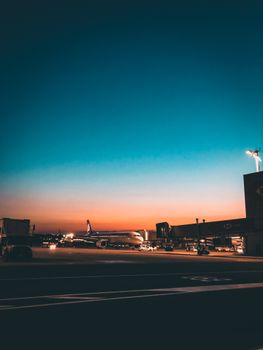 A stunning view of an airplane on the tarmac at dusk, against a vibrant sunset sky.