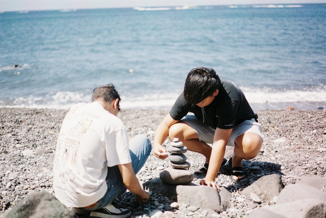 Young Men Balancing Rocks on the Beach