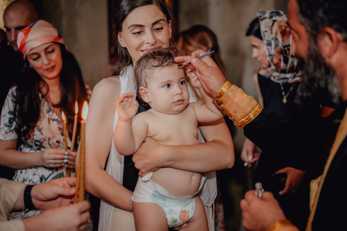 Free A touching moment during a baby's baptism ceremony surrounded by family and a priest. Stock Photo