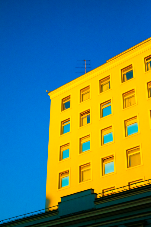 Free Low-angle view of a bright yellow building set against a clear blue sky, highlighting architectural details. Stock Photo