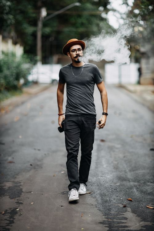 Free A stylish hipster man with a hat and mustache walking and smoking on a city street. Stock Photo