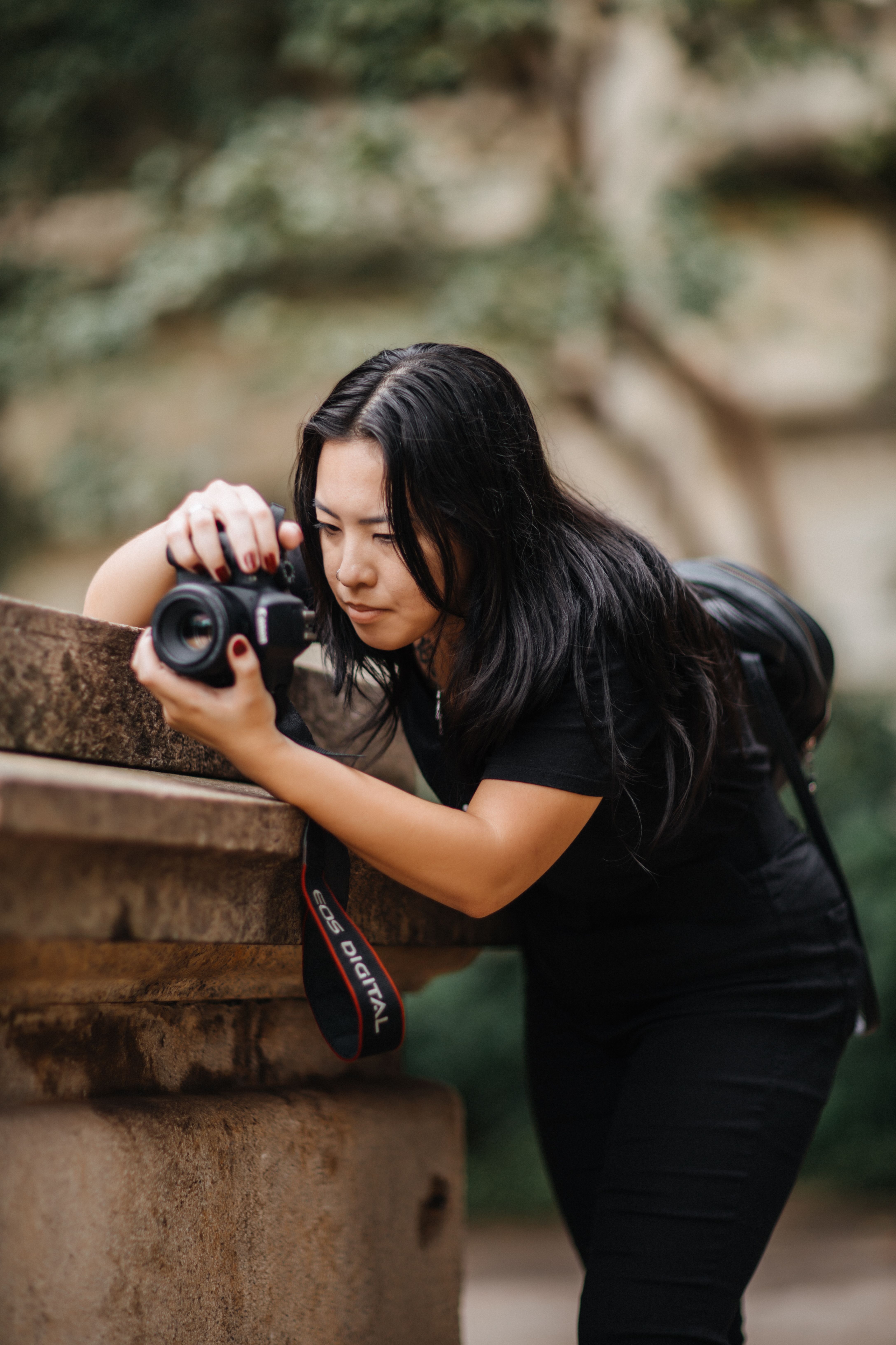 An Asian woman captures a scene with a camera outdoors, focused and intent.
