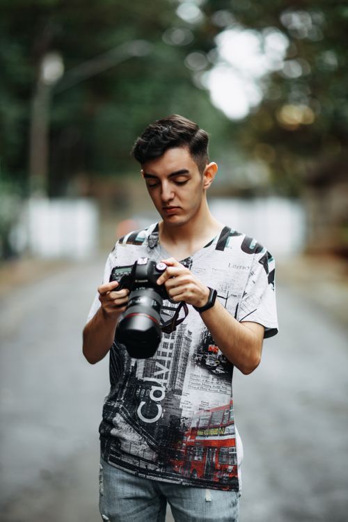 Free Young male photographer reviewing camera shots outdoors with a blurred background. Stock Photo