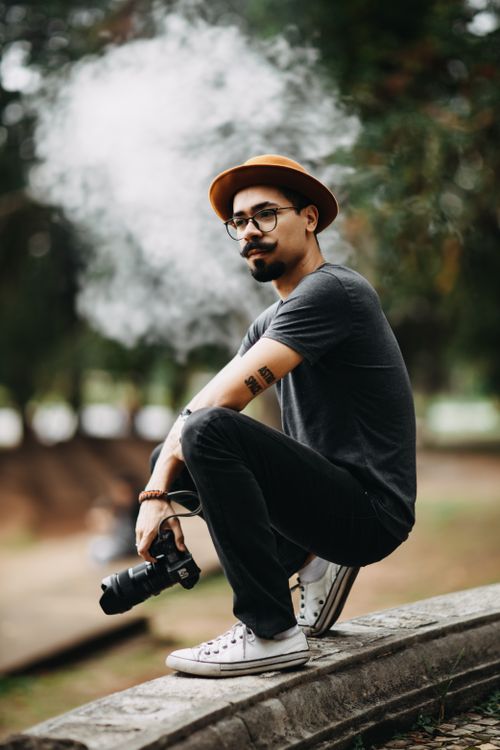 Free Casual young man sitting outdoors with a camera, exuding creativity and style. Stock Photo