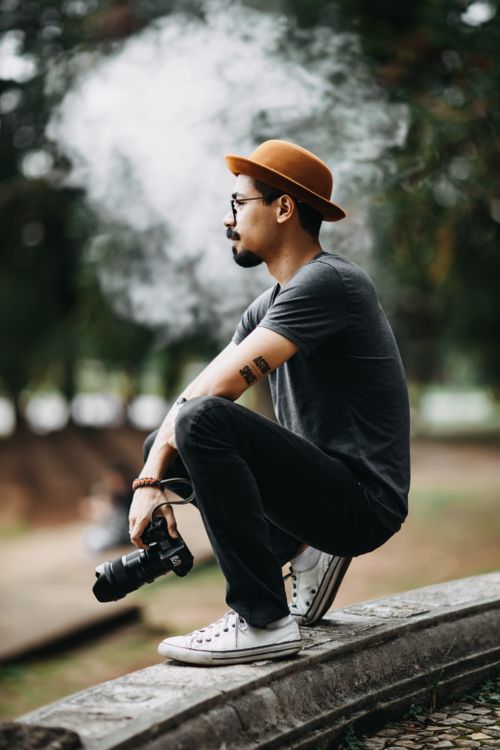 Free Side view of a man sitting and smoking outside, holding a camera. Stock Photo