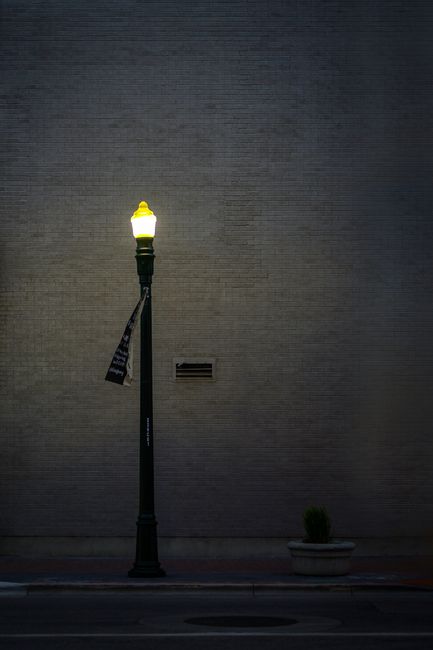 Atmospheric street scene featuring a lit lamp post against a textured brick wall.