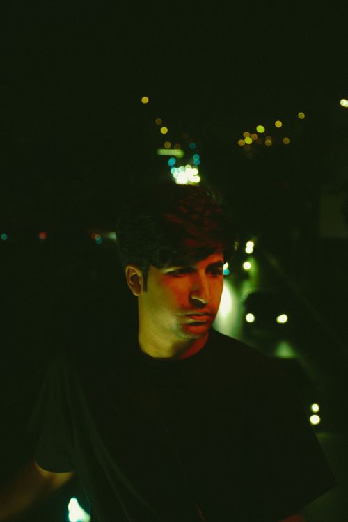 Free A moody portrait of a young man in a city street at night, illuminated by urban lights. Stock Photo