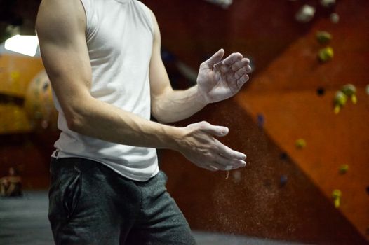 A climber applies chalk to his hands before rock climbing indoors, ensuring a better grip.