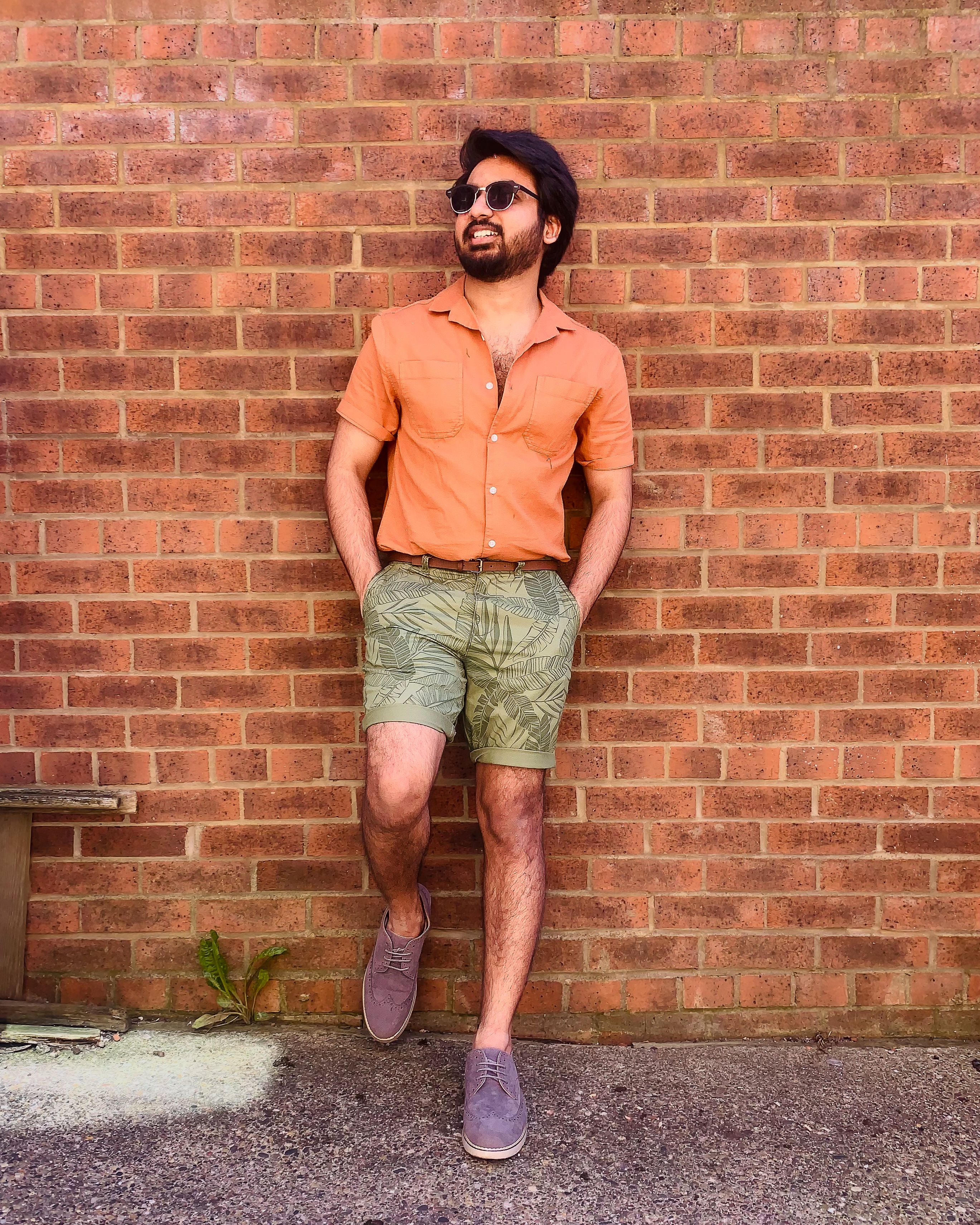 Retrato de moda casual de um homem em traje de verão contra uma parede de tijolos.