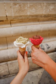 Two hands hold rose-shaped gelato cones in Malta, a taste of summer outdoors. by Kristina Paukshtite