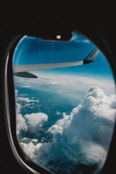 View of clouds and airplane wing through a plane window, capturing the essence of travel.