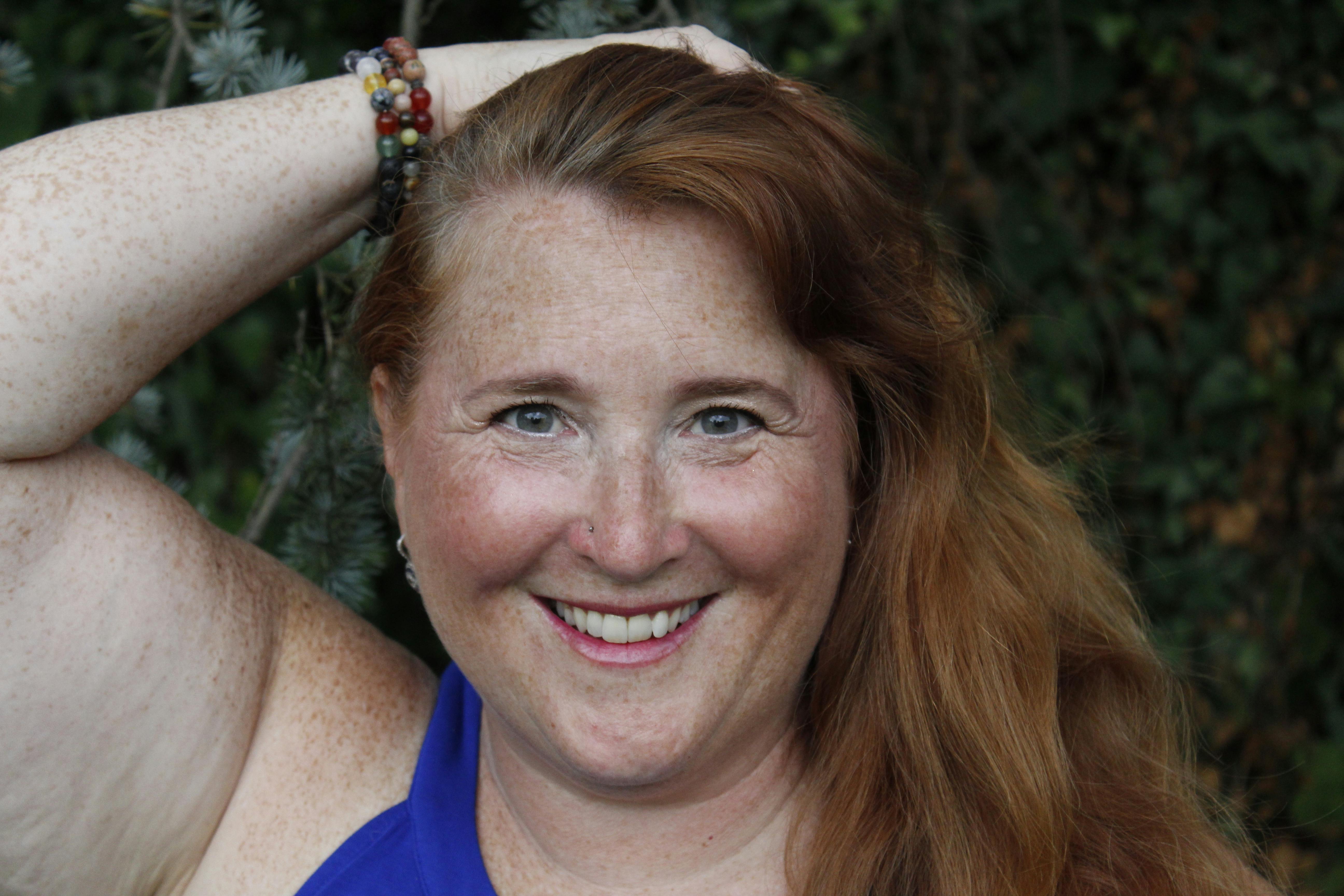 Happy woman with red hair and freckles smiling outdoors, showcasing natural beauty.