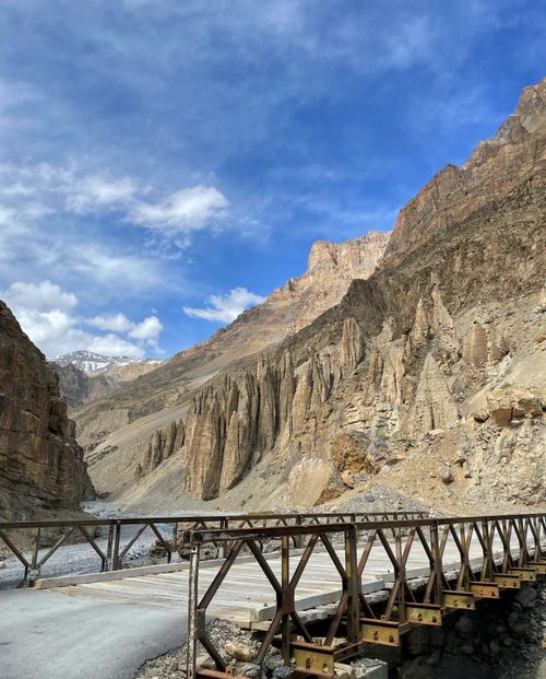 Free Rustic metal bridge over rocky riverbed in majestic mountain landscape under blue sky. Stock Photo