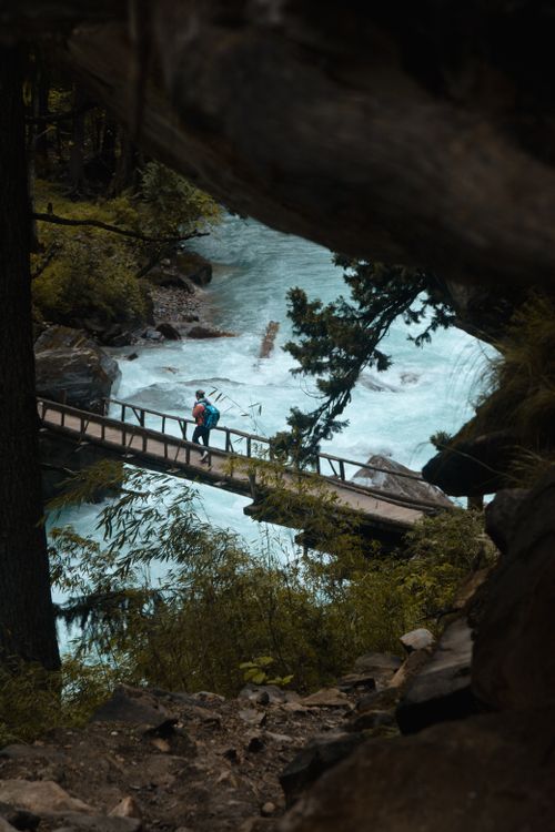 Free A lone hiker crosses a scenic wooden bridge over a flowing river in the mountains of Nepal. Stock Photo
