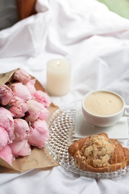 Cozy breakfast with coffee, croissant, and pink peonies on a bright morning.