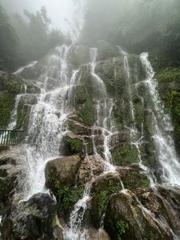 Capture of a scenic waterfall cascading over rocks, surrounded by mist and lush greenery.