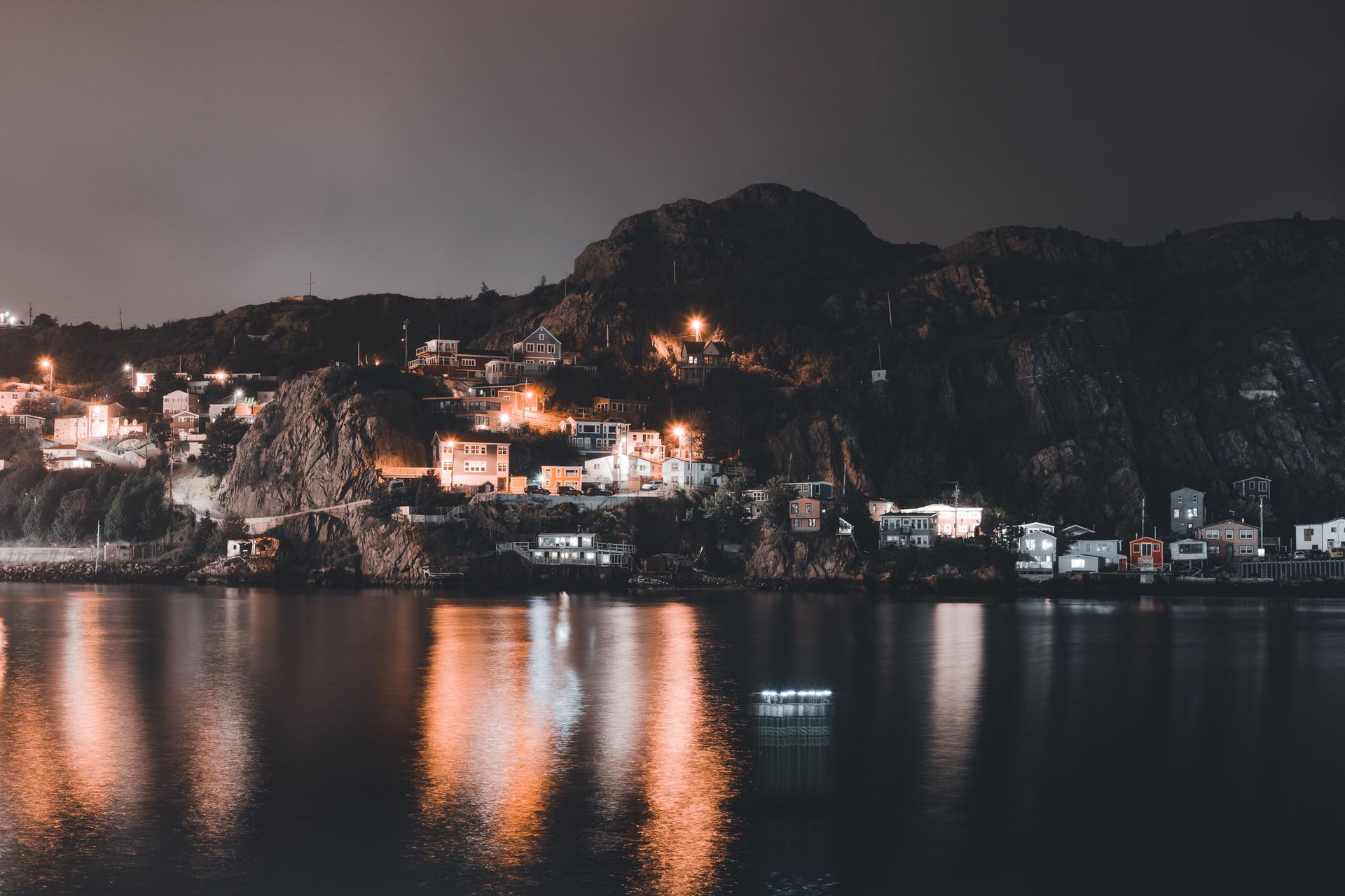 Serene night landscape of a coastal village with reflections on still water.
