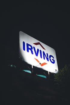 Close-up of a large illuminated Irving sign against a dark night sky.