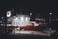 Illuminated Canadian icebreaker ship docked in a harbor at night with city lights in the background.