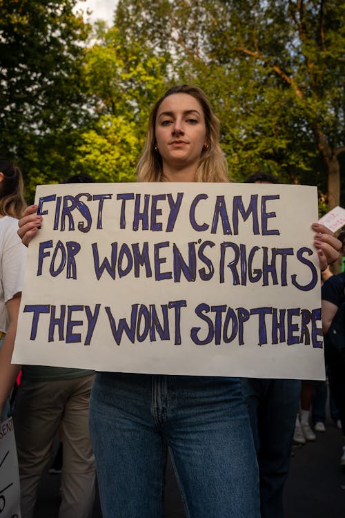 A Woman Holding a Cardboard with Message while Seriously Looking at the Camera