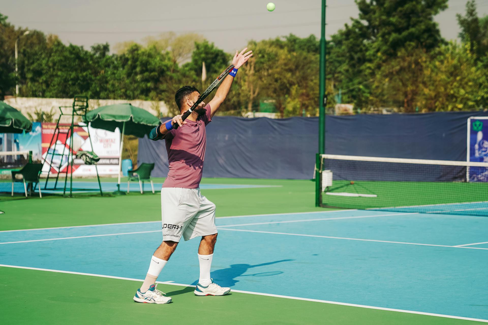 A focused tennis player serves on an outdoor court under clear skies in Islamabad, Pakistan.