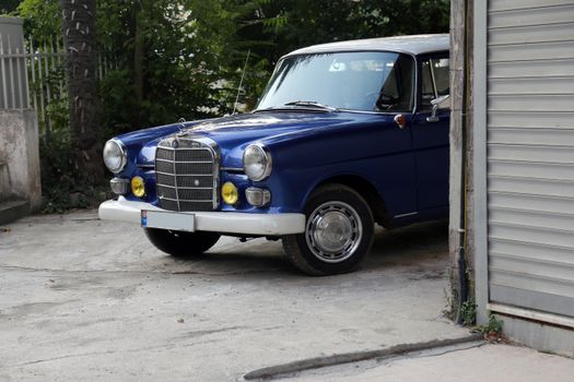 Blue vintage car partially parked in a garage, showcasing retro design and urban surroundings.