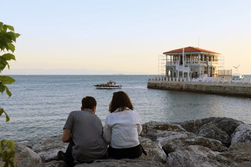 Man and Woman Sitting on a Rock Near Body of Water