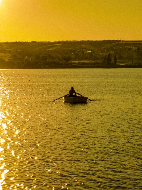 Free A lone rower navigates a boat during the serene golden hour, reflecting on peaceful waters. Stock Photo