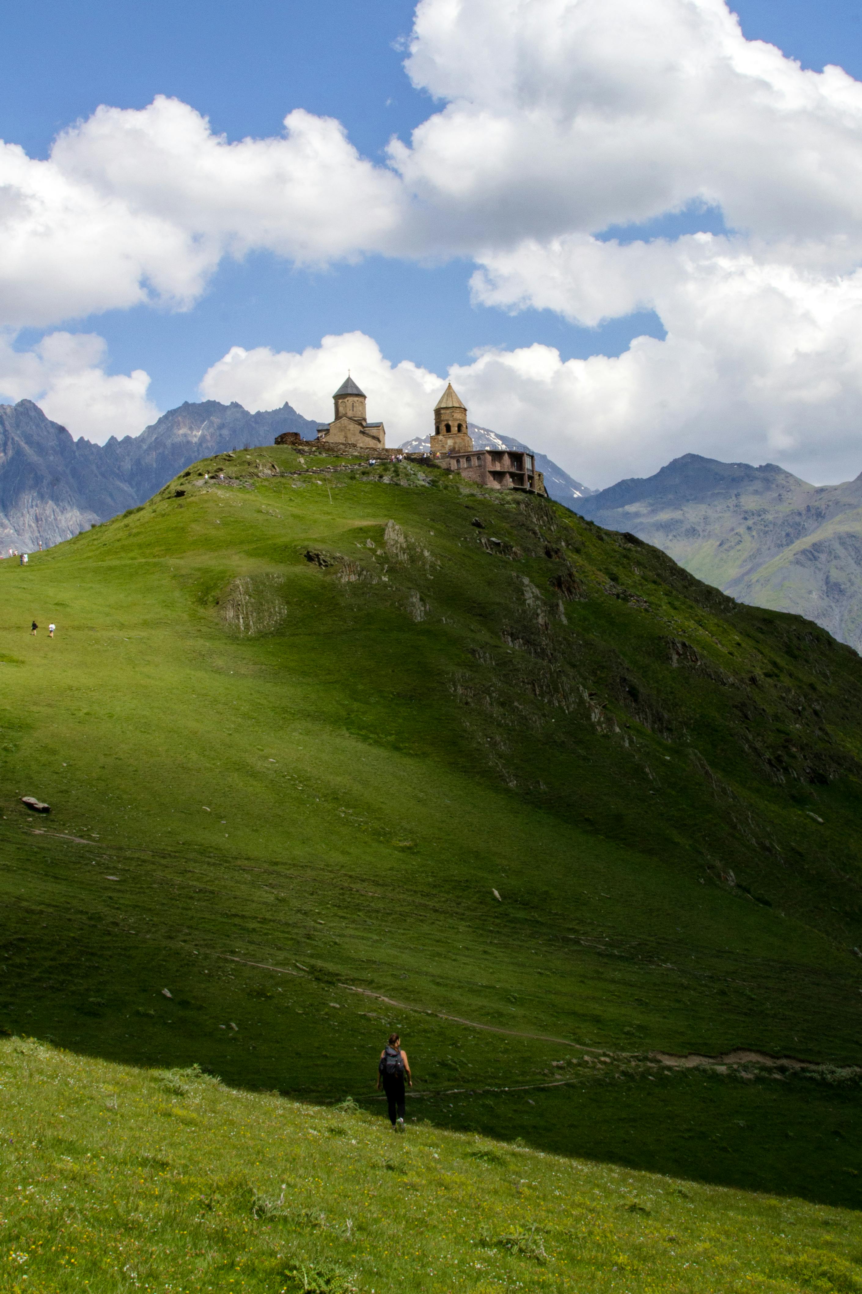 Scenic view of Gergeti Trinity Church atop a lush green hill in the Kazbegi region of Georgia.