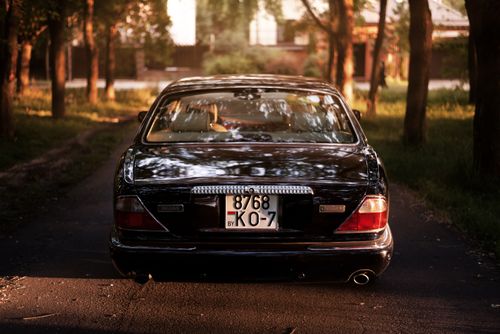 Free Luxurious black Jaguar car parked on a serene road lined with trees, showcasing elegance and style. Stock Photo