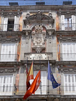 Front view of Casa de la Panadería's detailed facade with flags at Plaza Mayor in Madrid, Spain.