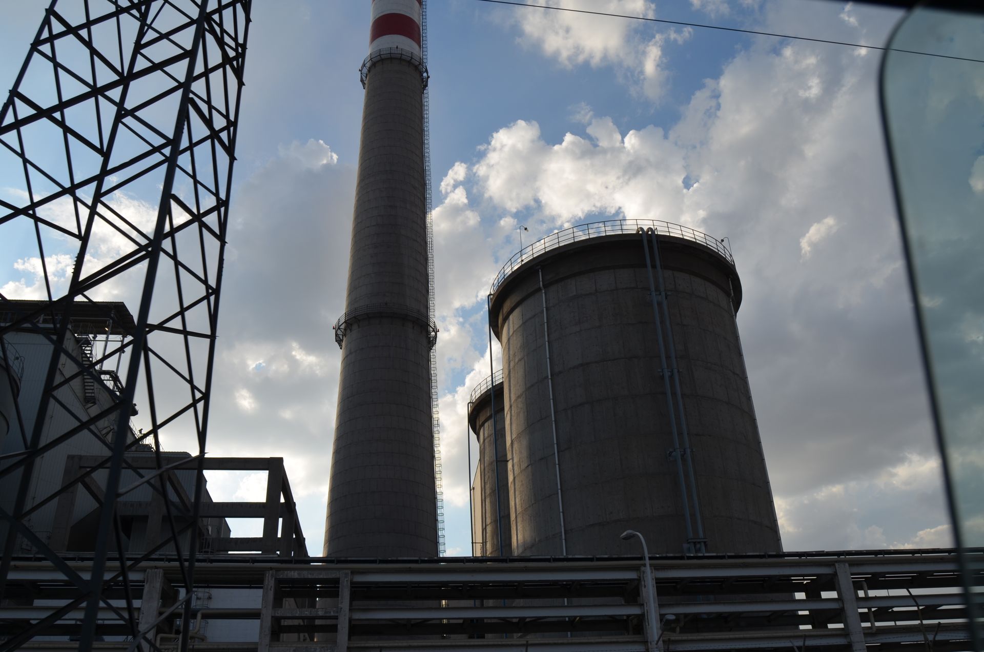 Low angle view of an industrial facility featuring a tall smokestack and structures under a cloudy sky.