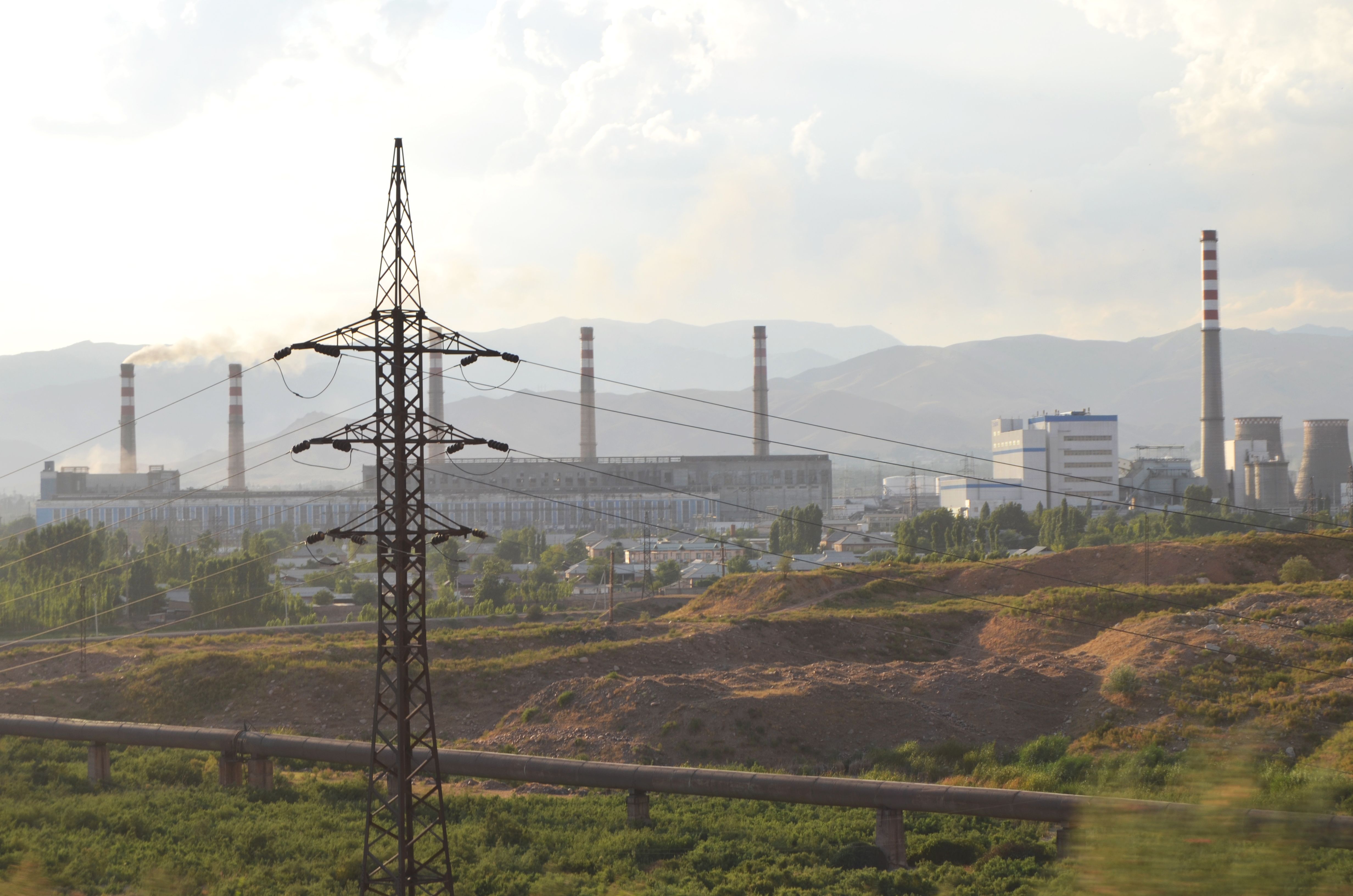 A view of an industrial power plant with an electricity pylon and smokestacks in the background.