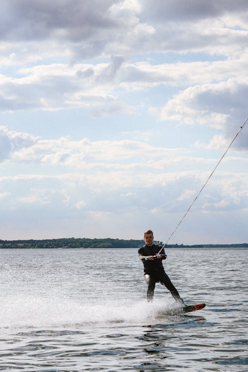 Free Man in Wetsuit Wakeboarding under a Cloudy Sky Stock Photo
