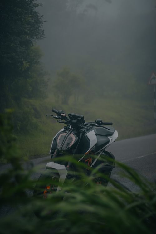 Free A motorcycle parked on a foggy road in Ponmudi, Kerala, India, surrounded by lush greenery. Stock Photo