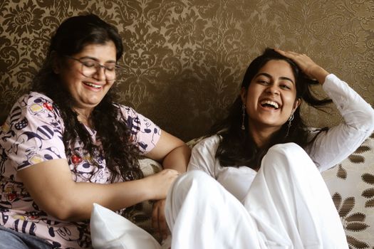 Two Asian women laughing and enjoying a moment together on a couch indoors.