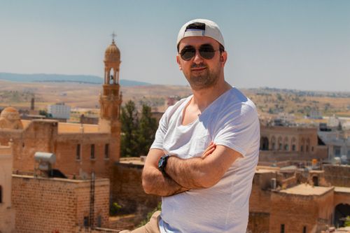 Free Man in white t-shirt and sunglasses posing near historic architecture on a sunny day. Stock Photo