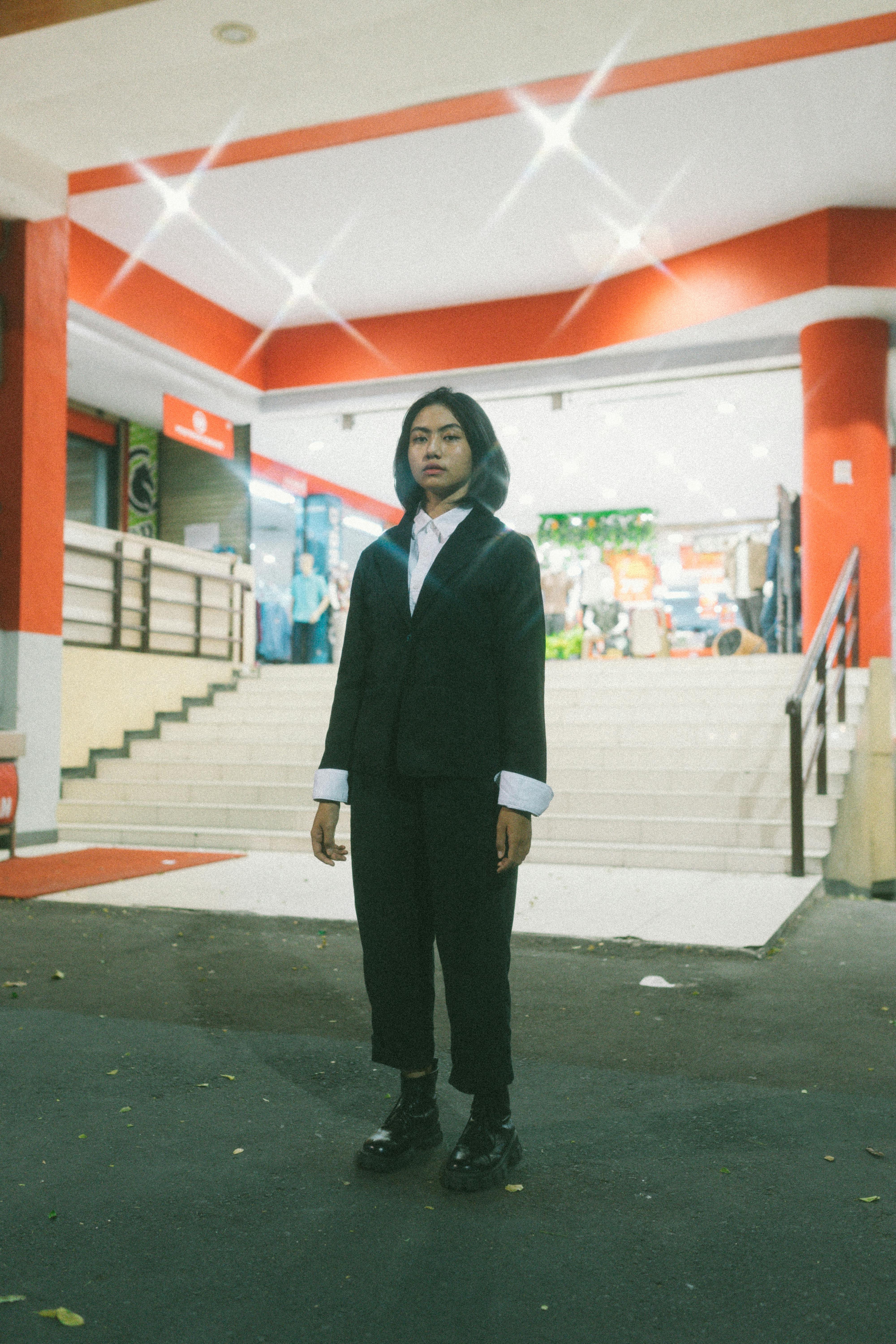 Young Asian woman in a formal suit standing outside a brightly illuminated modern building at night.