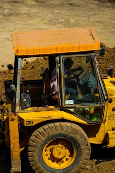 Close-up of a man driving a yellow bulldozer on a construction site during the day.