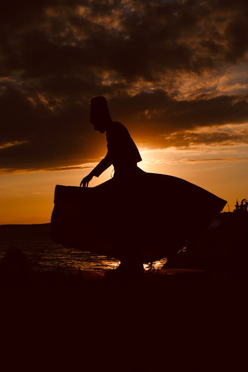 Silhouette of Person Standing on Rock during Sunset