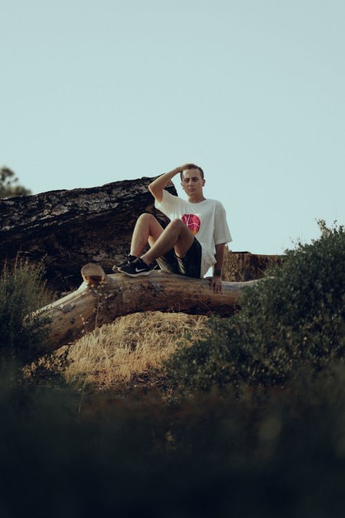 Free A man relaxes on a fallen tree in a serene outdoor environment. Stock Photo
