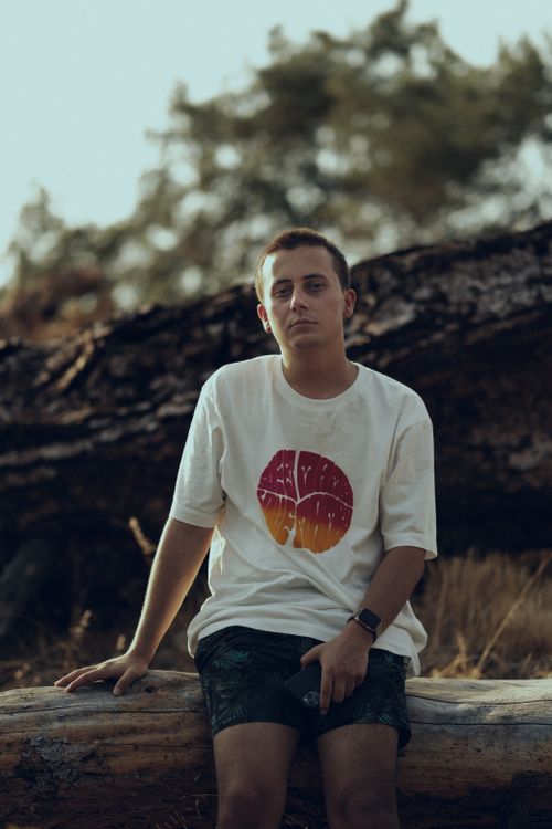 Free Casual portrait of a young man sitting on a log, enjoying leisure time outdoors. Stock Photo