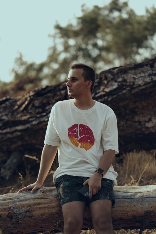 Free Portrait of a man in a white shirt sitting on a log in a natural outdoor setting. Stock Photo