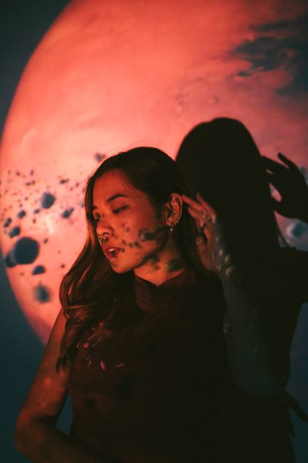 A young woman poses in front of a celestial backdrop, creating a dramatic artistic shadow.