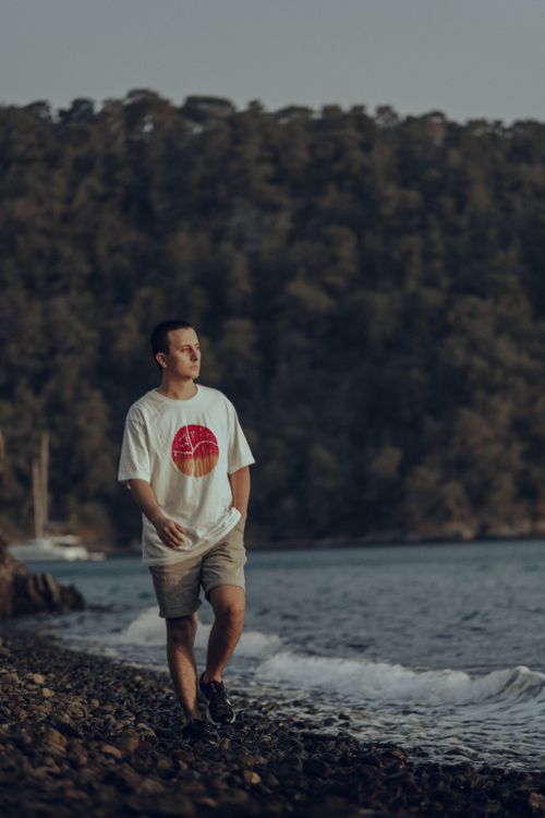 Free A man enjoys a leisurely walk on a rocky beach by the sea in summer. Stock Photo