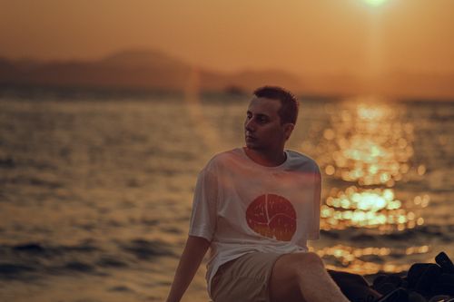 Free A man enjoying the scenic beauty of the ocean at sunset with reflective water. Stock Photo