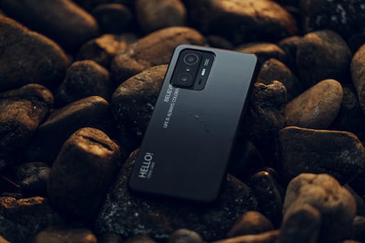 A smartphone rests on smooth pebbles, showcasing a modern design against a natural backdrop.