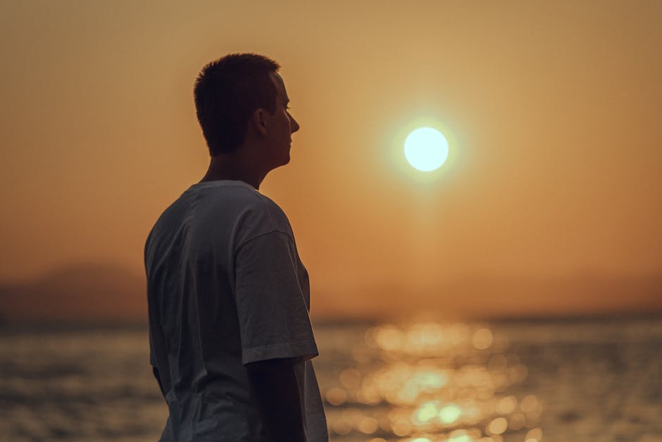 Silhouette of a man in a white shirt gazing at the ocean during sunset.