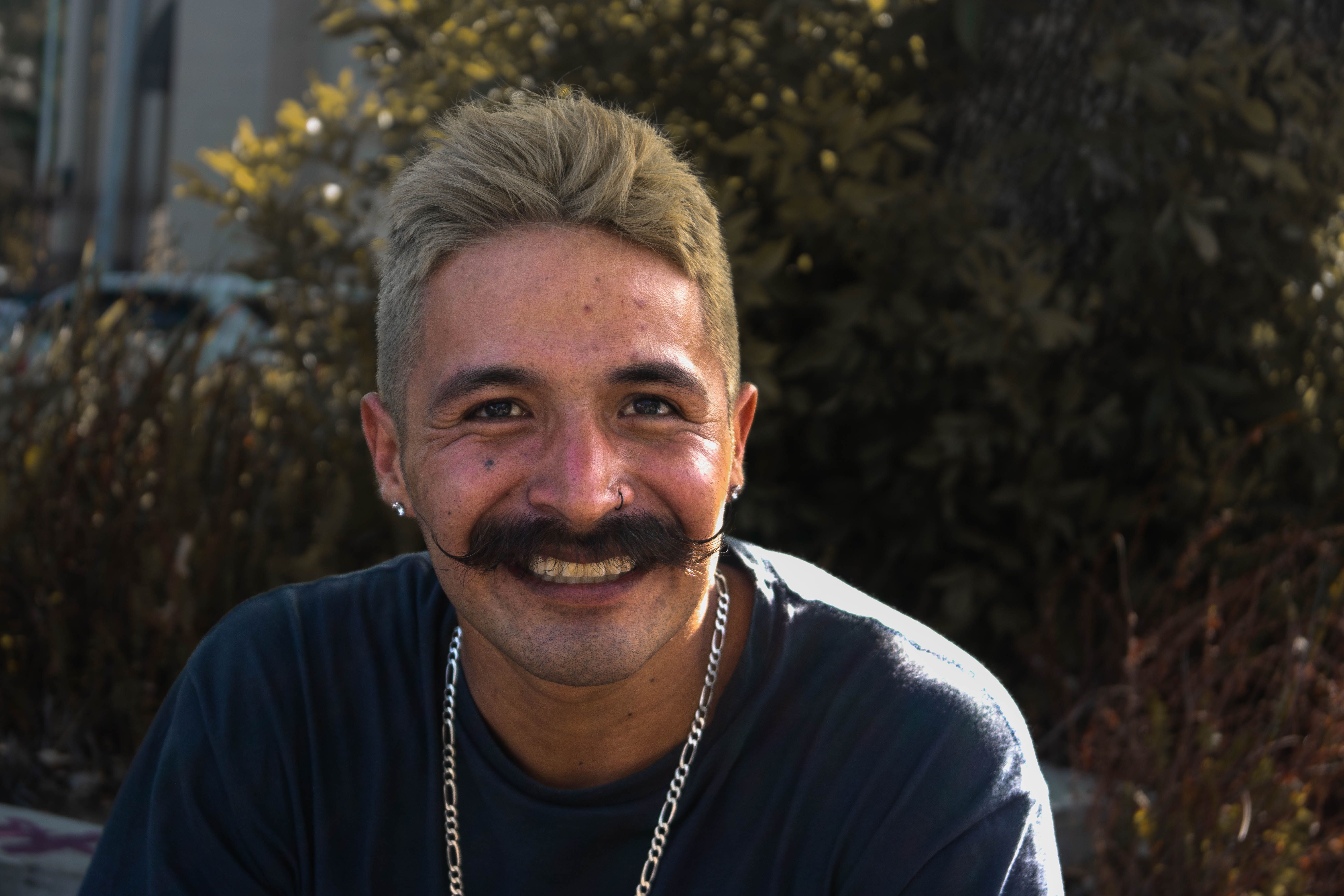Cheerful man with mustache and earrings smiling in an outdoor setting in Monterrey.