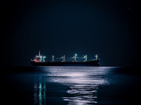 A tranquil nighttime scene of a cargo ship floating on a calm ocean under a starlit sky.